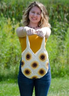 a woman holding onto a crocheted bag with sunflowers on the front