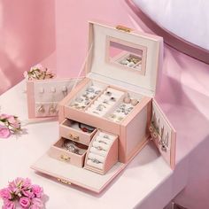 an open jewelry box sitting on top of a table with pink flowers in the background