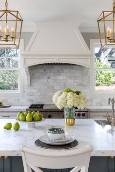 a kitchen with marble counter tops and white cabinets, surrounded by hanging lights over the stove