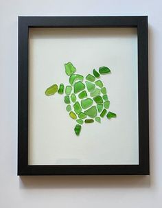 a sea turtle made out of sea glass in a black frame on a white wall