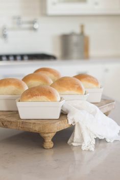 bread rolls sitting on a wooden tray in the middle of a kitchen counter with napkins