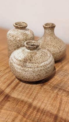 three small vases sitting on top of a wooden table next to each other,