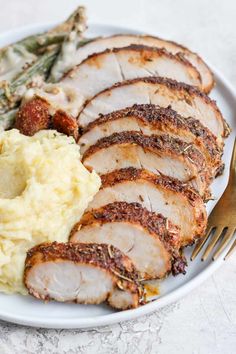 a white plate topped with meat, mashed potatoes and asparagus next to a fork