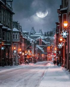 a city street with snow on the ground and buildings in the background, under a full moon