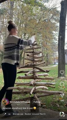 a woman standing next to a tree made out of sticks and logs in the woods