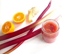 an assortment of fruits and vegetables on a white surface with a jar of liquid next to them