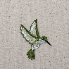 a green and white hummingbird flying over a beige fabric covered wall with stitching on it's back