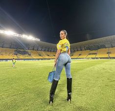 a woman standing on top of a lush green field in front of a stadium filled with people