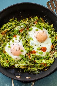 two fried eggs are in a skillet with green vegetables and seasoning on the side