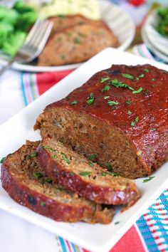 meatloaf with sauce and herbs on a white plate next to broccoli