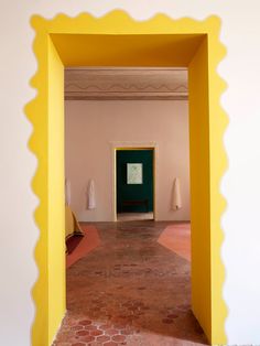 an open doorway in a room with red brick floors and white walls, leading to a painting on the wall