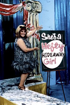 a woman standing next to a sign that says she's a happy hideaway girl