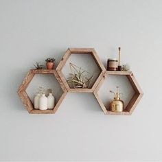 three wooden hexagonal shelves with plants and candles on them against a white wall