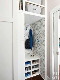 a white closet with shoes and purses on shelves next to a wallpapered door