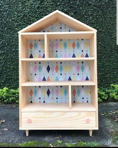 a wooden shelf with colorful geometric designs on the top and bottom shelves, sitting in front of a green wall