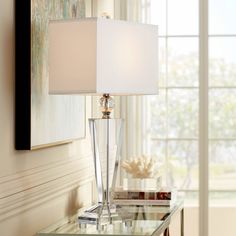 a glass table with a lamp on top of it next to a painting and window