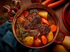 a pot filled with meat and vegetables on top of a wooden table next to carrots