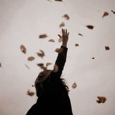 a woman reaching up into the sky with her hands in the air and falling leaves