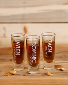 three shot glasses sitting on top of a wooden table next to nuts and almonds