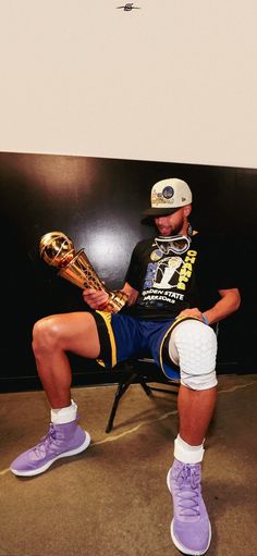 a man sitting in a chair holding a trophy and wearing purple shoes with white socks