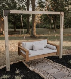 a wooden swing bed with pillows on it in the middle of a yard next to some trees