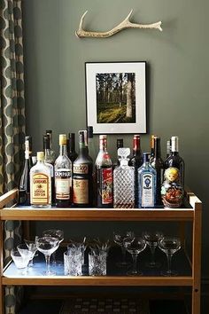 a bar cart with liquor bottles and glasses on it in front of a framed photograph