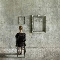 a woman sitting on a chair in front of a concrete wall with two square frames