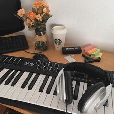 a keyboard with headphones on top of it next to a cup of coffee and flowers