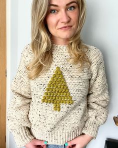 a woman standing in front of a wall wearing a sweater with a christmas tree on it