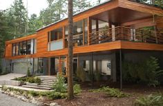 a large wooden house surrounded by trees in the middle of a forest with stairs leading up to it's second story