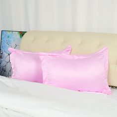 two pink pillows sitting on top of a bed next to a white headboard and pillow