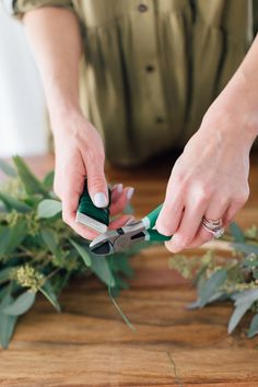 a woman is cutting up some flowers with scissors on a table next to greenery