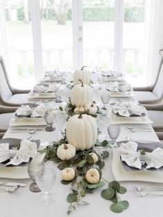 the table is set with white pumpkins, greenery and place settings for dinner