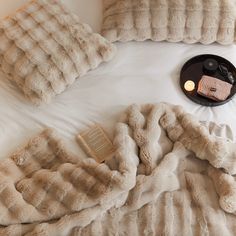 a bed topped with pillows and blankets next to a book on top of a table