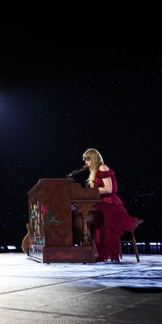 a woman in a red dress is sitting at a piano and singing into a microphone