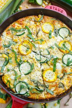 a pizza in a red pan on a wooden table next to corn and other vegetables