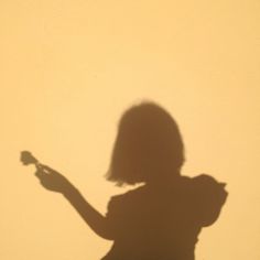 a shadow of a woman holding a cell phone in her hand and looking at the camera