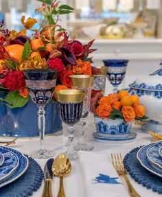 the table is set with blue and white dishes, silverware, and orange flowers