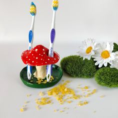 two toothbrushes sitting on top of a green plate next to flowers and grass