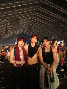 three young men standing next to each other in front of a crowd at an outdoor concert