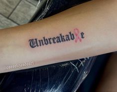 a person with a tattoo on their arm that says unbreakable and has a pink ribbon