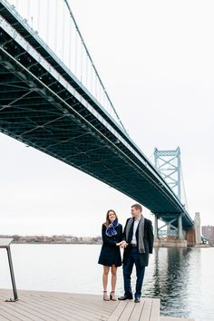 a man and woman standing on a dock next to a bridge