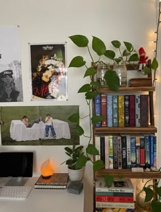 a computer desk with books, plants and pictures on the wall