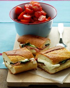 two sandwiches cut in half on a cutting board next to a bowl of tomatoes and a fork