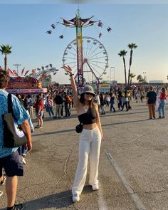 a woman standing in front of a ferris wheel at an amusement park with her hand up