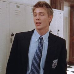 a young man wearing a suit and tie standing in front of lockers with his mouth open