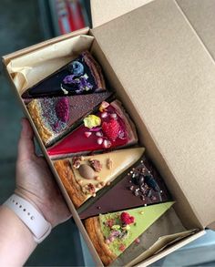 a person is holding an open box with different desserts in it