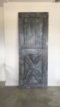 an old wooden door in the corner of a white walled room with concrete flooring