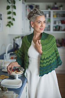 a woman standing in front of a counter holding a plate of food and wearing a green shawl