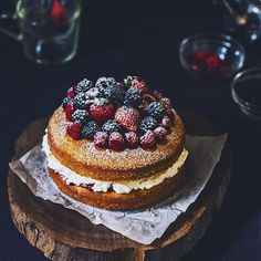 a cake sitting on top of a wooden platter covered in berries and whipped cream